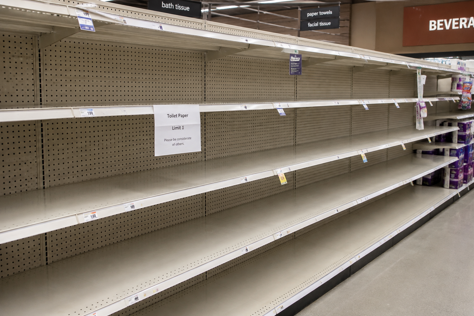 Empty store shelves with a sign reading Toilet Paper Limit 1 — Please be considerate of others