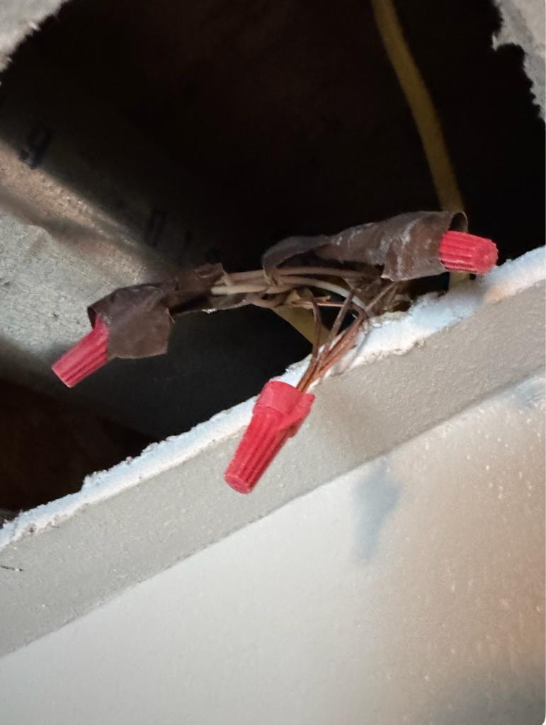 Electrical wire connections with red wire nuts exposed above a drywall opening