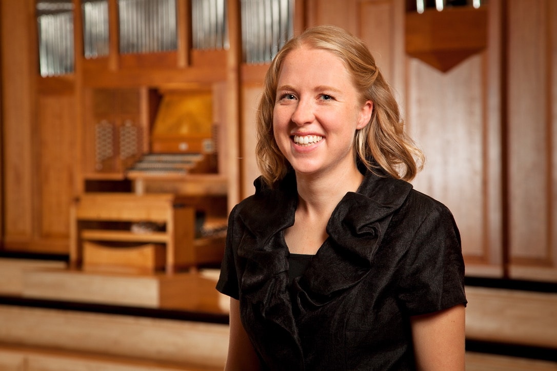 Mel smiling in front of a cathedral pipe organ — a musician whose humanity makes the music unforgettable.
